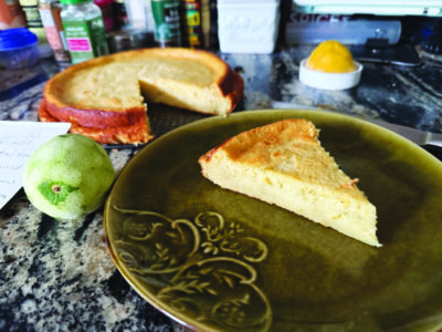 A slice of lime custard cake presented exquisitely with the rest of the cake in the background.