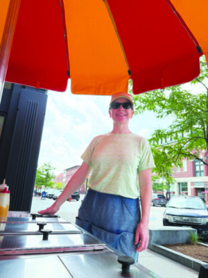 woman standings under orange and red awning, beside food bar, outside of small restaurant