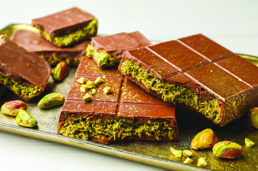 Pieces of Dubai chocolate bars with pistachios and knafeh on white table, closeup