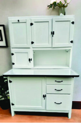 tall white piece of furniture standing on four legs with multiple drawers and cabinets, and a flat counter at mid height