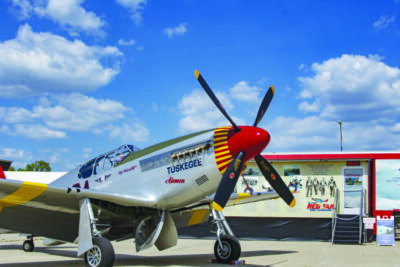small plane sitting on pavement in front of a traveling exhibit in a trailer, blue sky with clouds