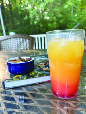 cocktail in tall glass, red at the bottom of the glass turning to yellow at top, sitting on table outside