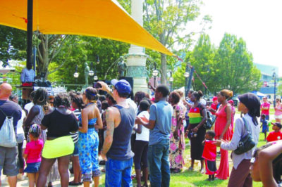crowd of people seen from behind as they stand outside on sunny day watching performance on outdoor stage