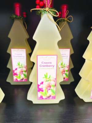 wine in a frosted glass bottle shaped like a christmas tree, sitting on a shiny surface with other bottles, festive holly decorations tied in twine at the top of each bottle