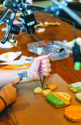 close up of a woman's hand holding a bag of icing as she decorates sugar cookies