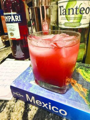 red cocktail with ice in a short ball glass sitting on a travel book about Mexico