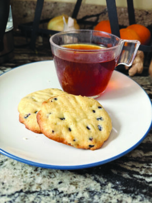 plate on counter holding clear glass tea cup and two blueberry cookies