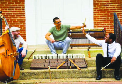 two white men and a black man sitting on concrete steps with their instruments