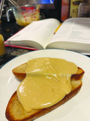 two pieces of toast covered with a cheese gravy on a plate, recipe book on counter behind