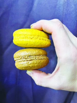 hand holding a brown and a yellow macaron