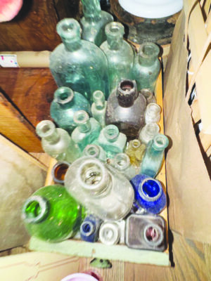 box of old, clouded glass bottles of various sizes and colors, in dim closet, photo taken from above