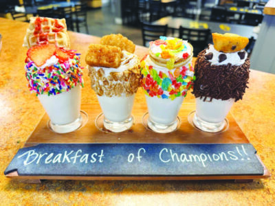 four milkshakes in small glasses frosted on the sides with different colorful sprinkles and different sweet toppings