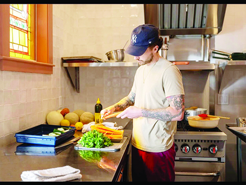 man standing in kitchen at large counter, prepping vegetables