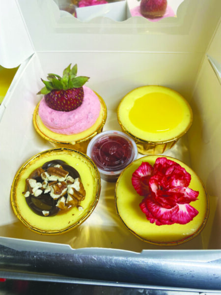 square bakeshop takeout box with four cupcake sized cheesecakes with different toppings