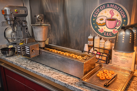 Counter with long doughnut making machine, doughnuts on conveyer belt