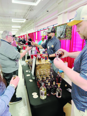 two men behind a table full of liquor samples, pouring out small samples for people at an indoor event