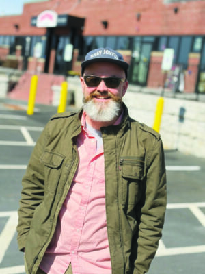 man with beard standing outside in parking lot, wearing sunglasses and baseball cap