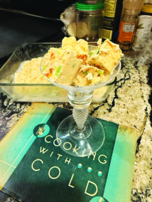 stemmed cocktail glass holding squares of frozen peanut butter with suspended peppers, sitting on top of book called Cooking with Cold