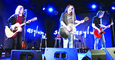three guitar players standing on stage in front of microphones