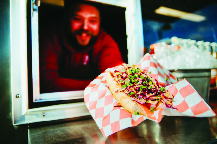 man leaning out of a window holding out a loaded hot dog in a bun