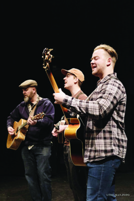 three men playing guitars on dark background