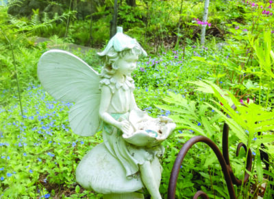 stone sculpture of garden fairy sitting on rock while reading book, sculpture in grassy area of garden