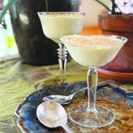 two stemmed, fancy cocktail glasses filled with tapioca and sitting on table beside plants