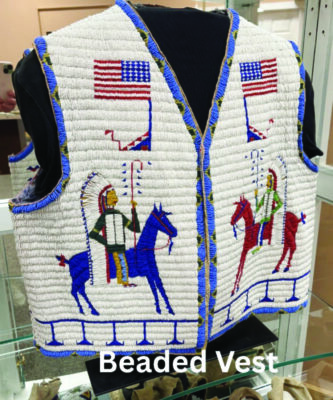 beaded best on display, decorated on each side with an image of a man wearing a headress and holding a staff, riding a horse, USA flags above them. 