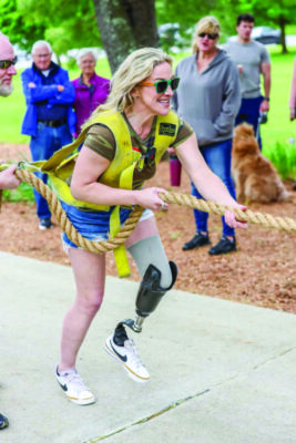 woman with one prosthetic leg, pulling on rope, on sidewalk while people gather