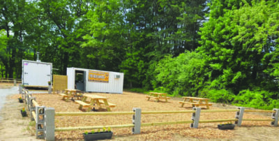 area enclosed in temporary fence made of cement blocks and wood, filled with wood chips, containing picnic tables and a shipping container made into a concession stand