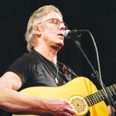 gray haired man playing guitar and singing into microphone