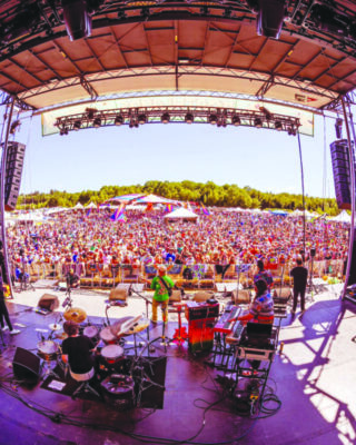 looking out from outdoor stage at back of band and to standing audience on sunny day