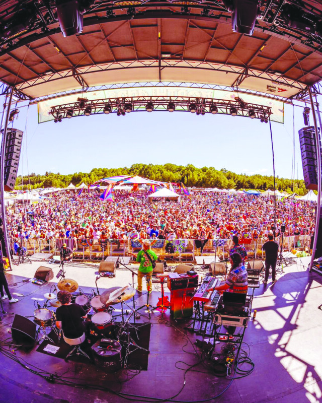 looking out from outdoor stage at back of band and to standing audience on sunny day