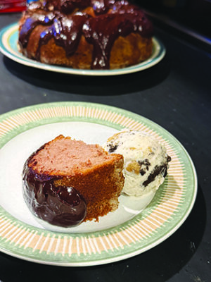 slice of round cake with thick chocolate ganache on plate beside scoop of ice cream