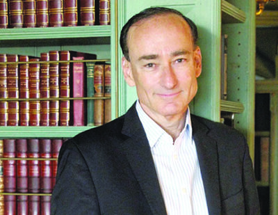 head shot of mature white man standing in front of bookcase with leather bound books