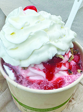 seen from above, a cup of ice cream topped with strawberries and whipped cream, with a cherry on top