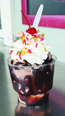 Ice cream sundae in a clear plastic cup with chocolate sauce coating the sides, whipped cream, sprinkles and a cherry on top