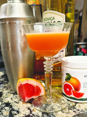 cocktail glass on counter beside cut grapefruit and cocktail shaker