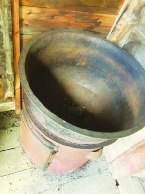 large metal cauldron on top of metal cylindrical wood fired stove, seen from above.