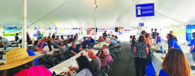 people eating at folding tables under large tent, food vendor tables along side