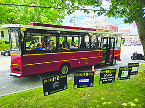 red trolly on street, beside grassy area with lawn signs promoting UFO festival