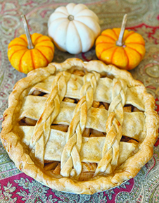 close up of pie, seen from the top with lattice crust, beside three small decorative pumpkins