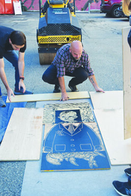 men arranging carved boards on the ground to be printed under small steamroller