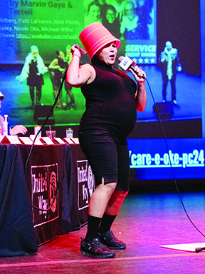 woman on stage wearing bucket on her head, holding microphone and singing