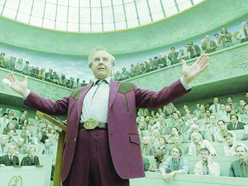 screenshot from Digger showing man in suit with big belt buckle and string tie proclaiming in front of large audience in rotundra