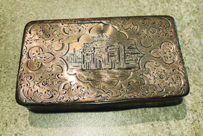 small metal box with top engraved with decorative border around a building