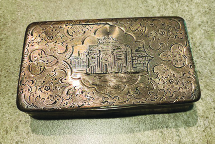 small metal box with top engraved with decorative border around a building